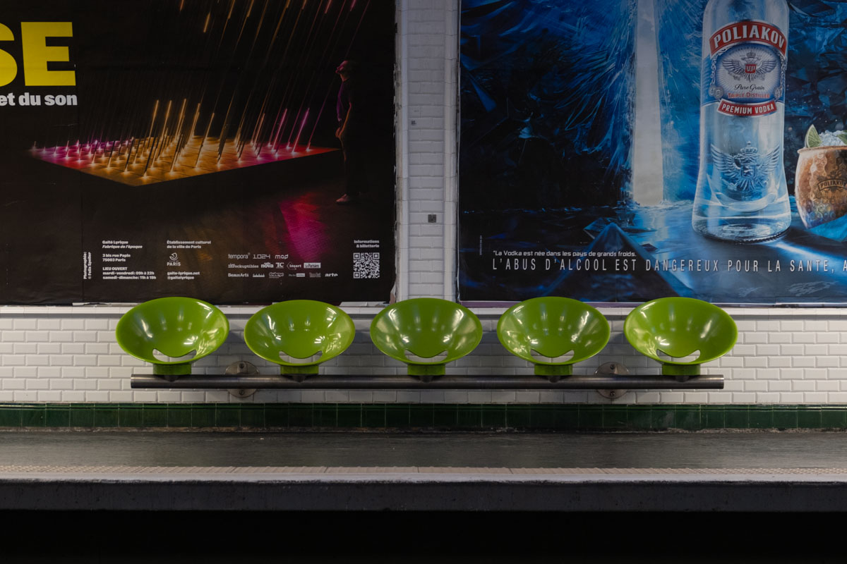 Homeless people sheltering inside a fenced urban space under a Paris flyover, 2024
