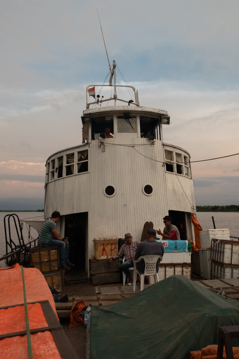 Crew and passengers unloading a motorcycle down a wooden plank from the Aquidaban at a remote riverside stop at sunset