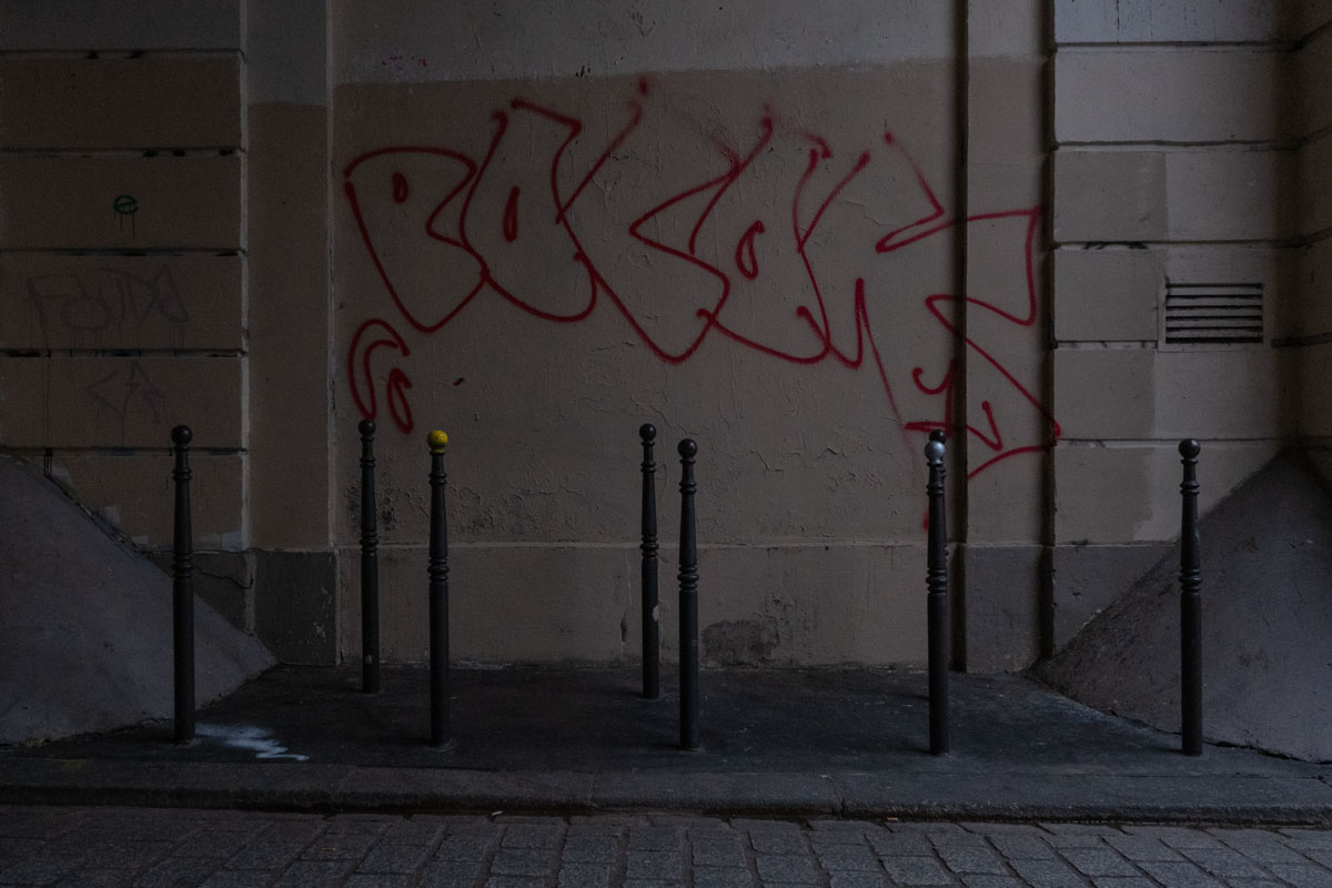 Empty bench on a quiet Paris street in autumn, with two figures walking in the distance