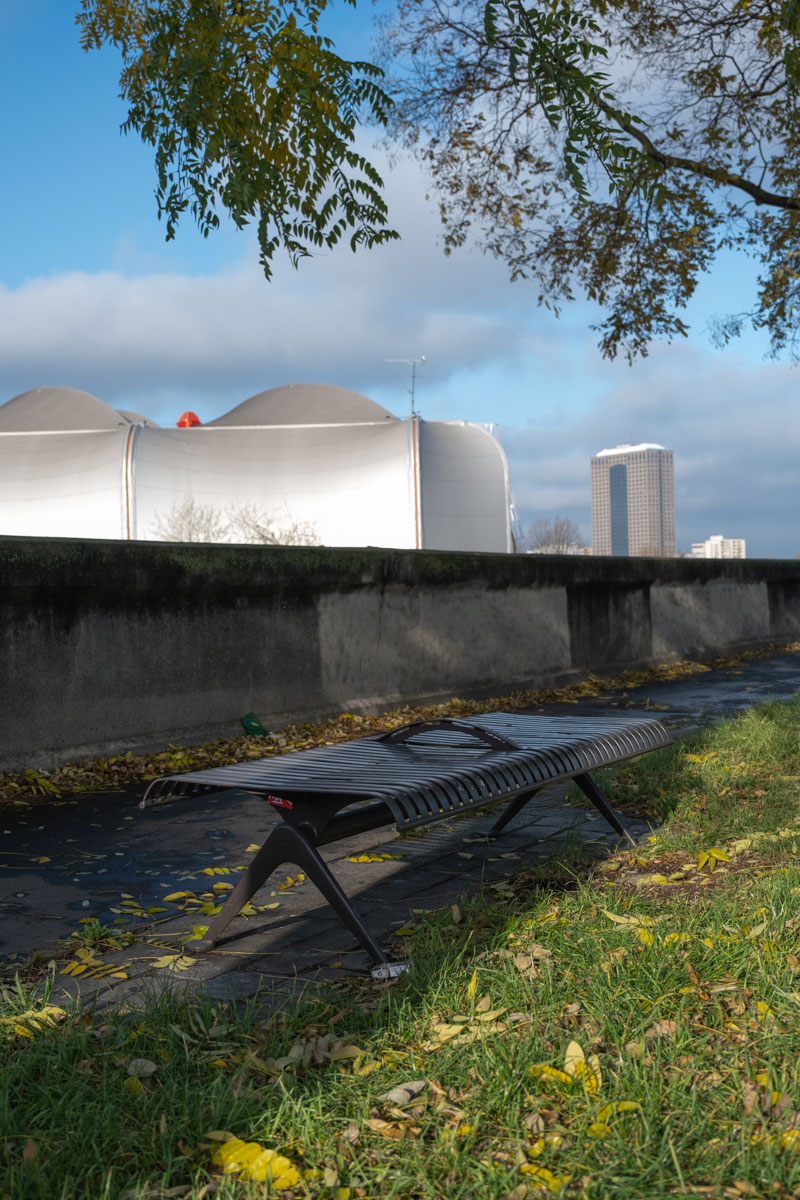 Graffiti-covered arched tunnels behind a metal fence at the base of a Paris bridge, autumn 2024