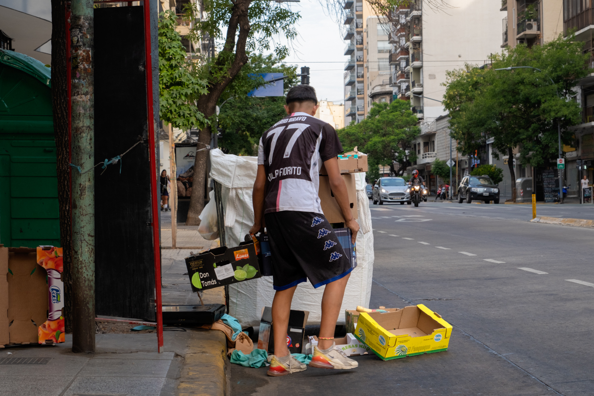 Three men sorting cardboard and waste bags beneath a tree on a Buenos Aires boulevard