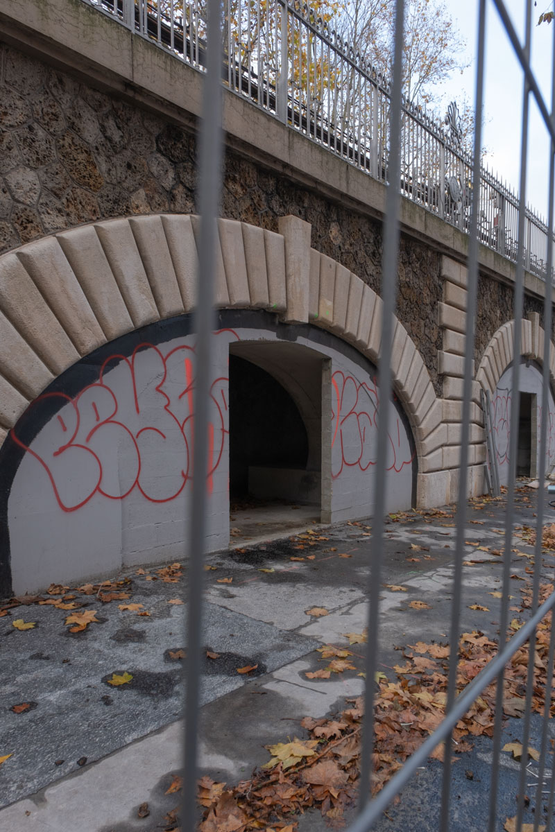 Anti-homeless bench on a Paris waterfront with industrial silos and a tower block in the background