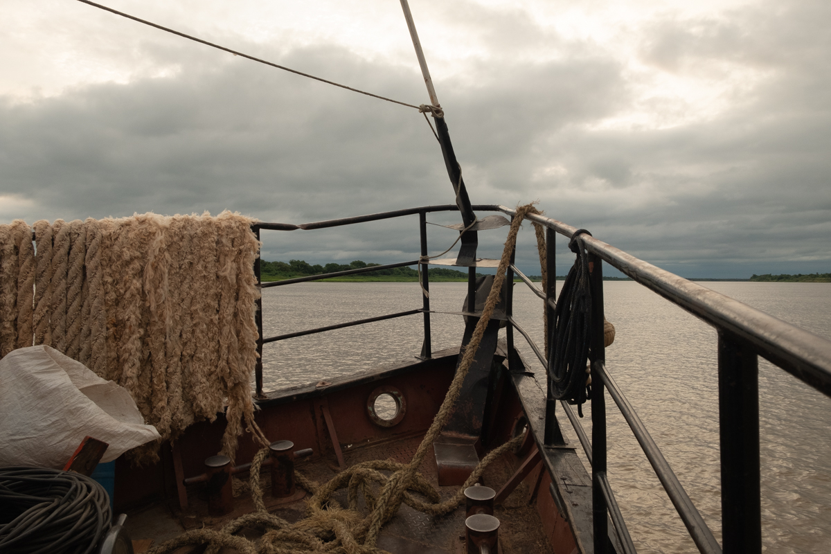 Man sitting on a wooden chair checking his phone beside a 'Sanitario' sign in the hold of the Aquidaban