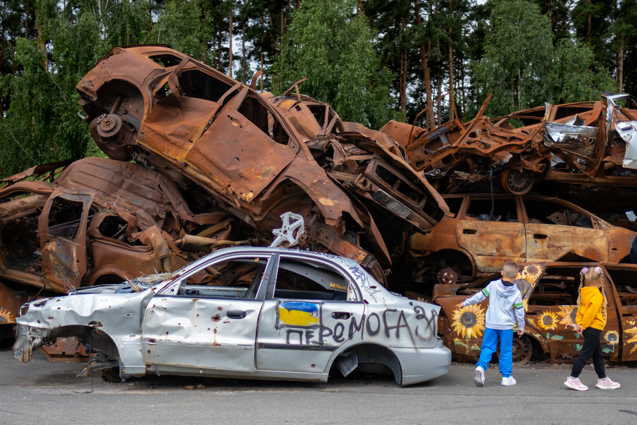 Documentary photography showing car junkyard scene with people and sunflowers